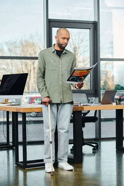 Homme handicapé se tient debout avec une canne à pied devant un bureau, tenant des tableaux dans un cadre de bureau. — Photo de stock