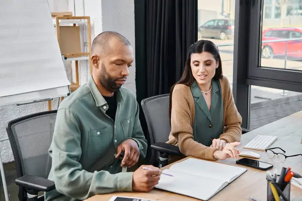 A man with eye syndrome and a woman deep in discussion at a table, working on a project in an office setting. — Stock Photo