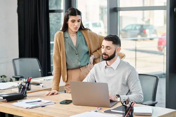 Ein Mann und eine Frau führen eine produktive Diskussion, während sie in einem modernen Büroumfeld auf einen Laptop blicken. — Stockfoto