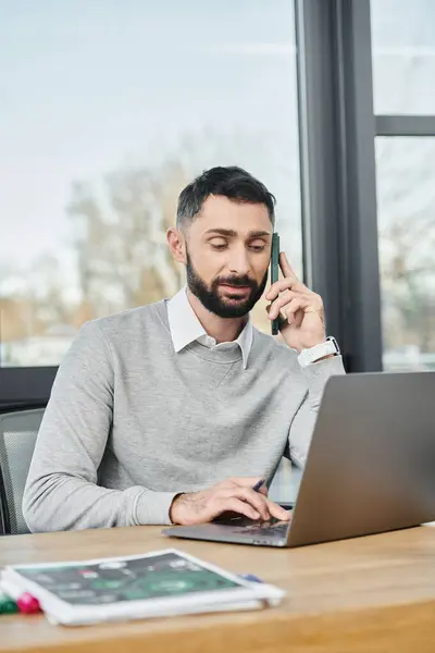 Un hombre en un entorno de negocios, sentado en una mesa ocupada en una llamada telefónica. - foto de stock