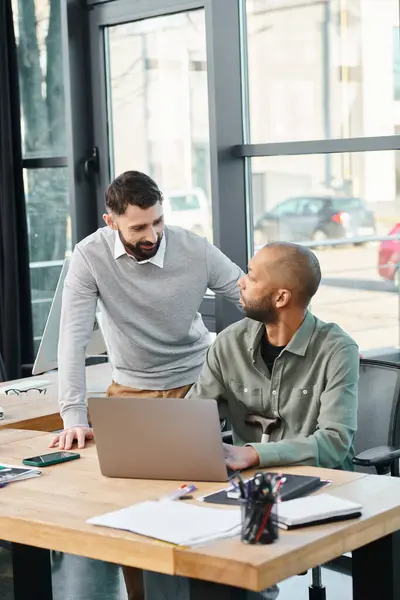 Two businessmen sitting at a table, focused on a laptop screen, engrossed in a corporate project discussion, diversity and inclusion — Stock Photo