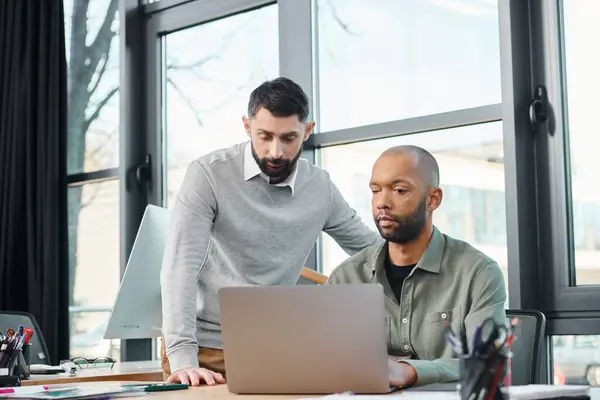 Two men in a corporate office are focused on a laptop screen, actively engaged in a discussion or project analysis, diversity and inclusion — Photo de stock