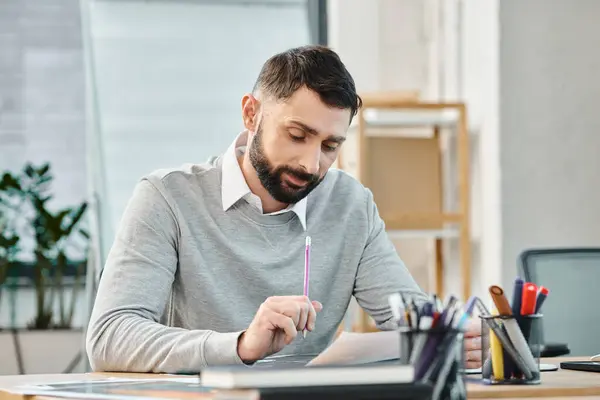A man sitting at a desk, focused, with a pen in his hand, working on a project in a bustling office setting. — Stock Photo