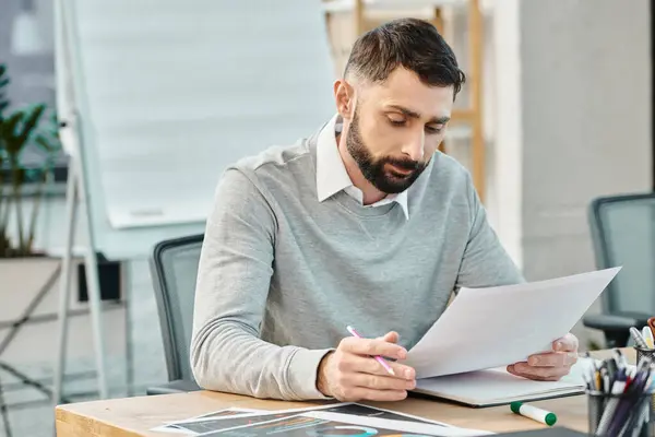 Мужчина в деловой одежде, сидящий за столом, интенсивно сосредоточенный на написании заметок ручкой на листе бумаги. — стоковое фото