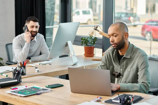 Dos profesionales de negocios se sientan en una mesa en una oficina trabajando en sus computadoras portátiles, enfocados y comprometidos en su proyecto. - foto de stock
