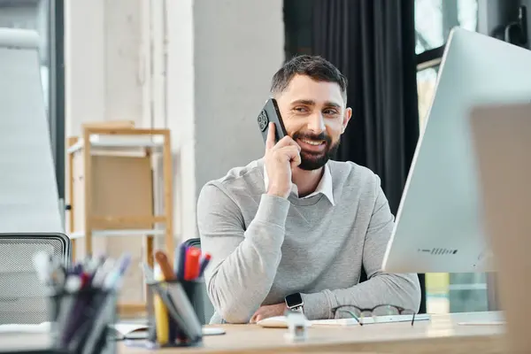 Un hombre absorto en una llamada mientras está sentado en su escritorio en un entorno de oficina, parte de un equipo centrado en un proyecto. - foto de stock