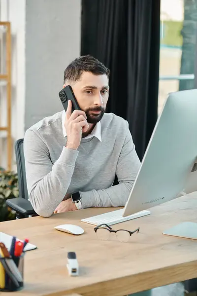 Ein Mann, der tief in ein Gespräch auf einem Handy vertieft ist, während er an einem Schreibtisch in einem Firmenbüro sitzt. — Stockfoto