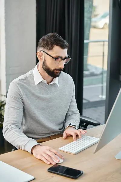 Un hombre sentado en un escritorio, profundamente absorto en el trabajo, usando una computadora para navegar a través de un proyecto para una asignación corporativa. - foto de stock
