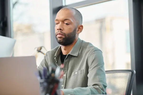 Un hombre discapacitado sentado frente a una computadora portátil en una oficina corporativa, enfocado en trabajar en un proyecto de negocios. - foto de stock