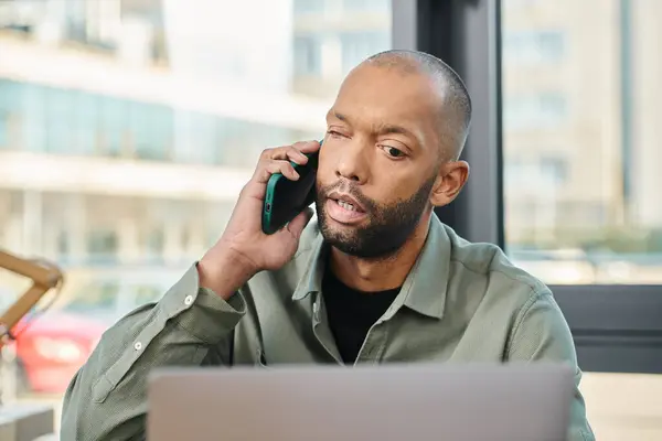 Disabled man with myasthenia gravis sits in front of a laptop, engaged in a phone call, embodying a multitasking digital age worker in a corporate setting. — Stock Photo