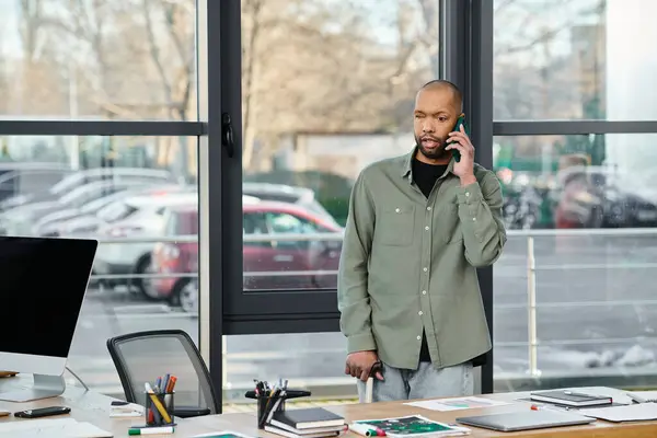 A man with myasthenia gravis in business attire talking on a cell phone while standing in front of a desk in an office setting. — Photo de stock