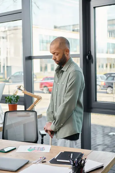 Un hombre con miastenia gravis en un entorno de oficina moderno, de pie con confianza frente a una computadora portátil, absorto en su trabajo. - foto de stock