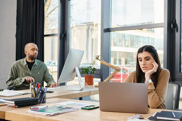 A man and a woman sit at a table in an office, focused on a laptop screen, working together on a business project. — Stock Photo