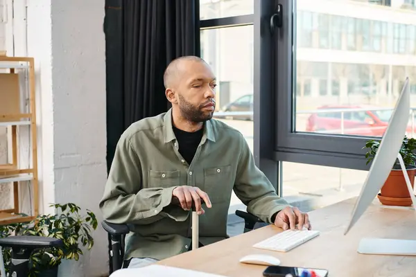 Un homme afro-américain handicapé atteint de myasthénie grave s'est concentré sur son écran d'ordinateur, tapant sur un clavier, créant un projet numérique dans un cadre de bureau d'entreprise. — Photo de stock
