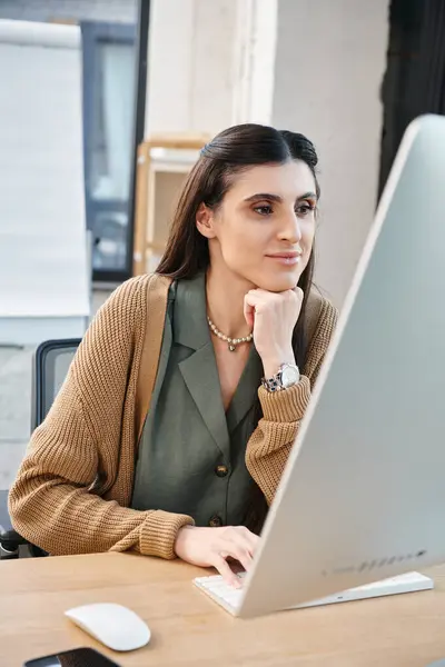 Una donna assorta nel lavoro, seduta davanti al suo computer portatile in un ufficio aziendale. — Foto stock