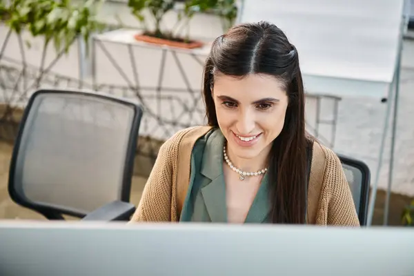 Uma mulher imersa no trabalho, focada em sua tela de computador em um ambiente de escritório movimentado. — Fotografia de Stock
