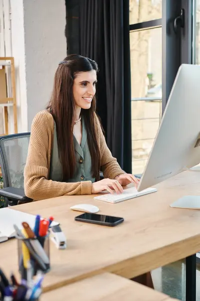 Uma mulher sentada em uma mesa, absorvida em seu laptop, envolvida no trabalho para um projeto corporativo. — Fotografia de Stock