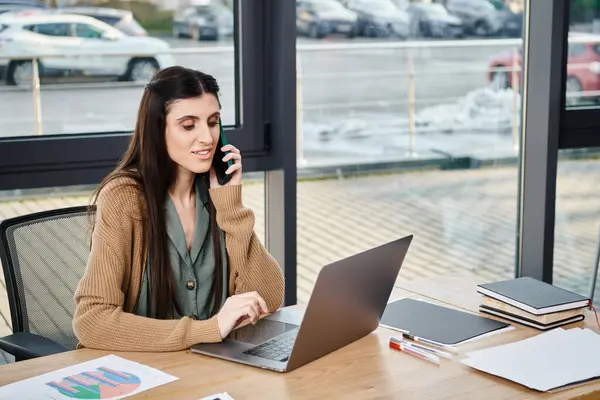 Uma mulher em um escritório corporativo se senta em uma mesa envolvida em conversa em um telefone celular. — Fotografia de Stock