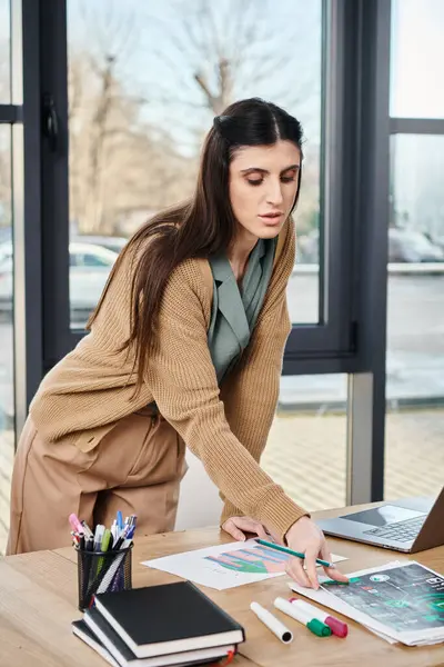 Uma mulher em trajes casuais de negócios trabalhando em um laptop em uma mesa de escritório moderna, imersa em um projeto. — Fotografia de Stock