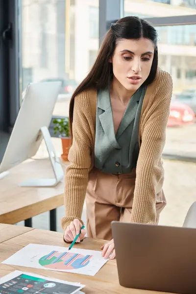 Une femme immergée dans le travail, assise à une table, tapant sur son ordinateur portable dans un cadre de bureau moderne et lumineux. — Photo de stock