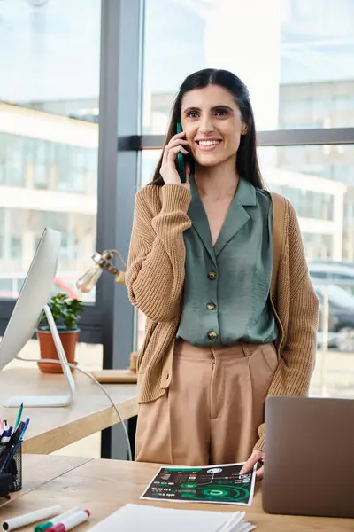 A woman standing confidently in front of a desk, actively engaged in a phone conversation while immersed in a corporate setting. — Photo de stock