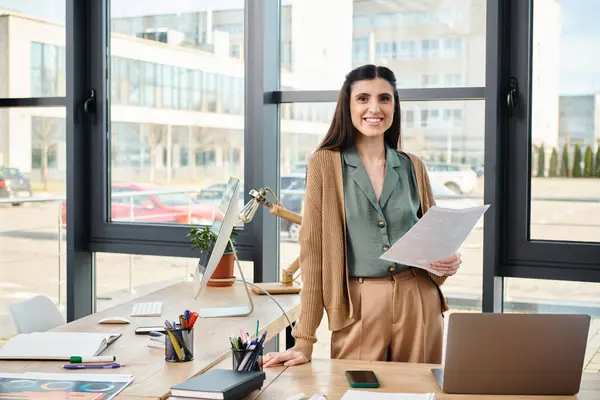 A professional woman standing at a desk with a laptop, immersed in a corporate project in a modern office setting. — Stock Photo