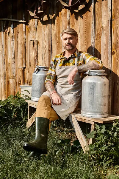 Granjero guapo en atuendo casual con tatuajes sentados con batidos de leche y mirando a la cámara - foto de stock