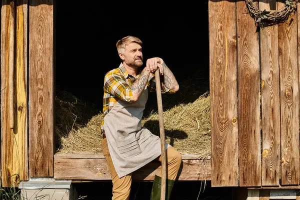Привлекательный преданный фермер в повседневной одежде, используя вилы во время работы с сеном в деревне — стоковое фото