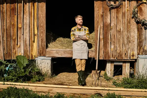 Atractivo agricultor dedicado en atuendo casual usando horquilla mientras trabaja con heno en la aldea - foto de stock
