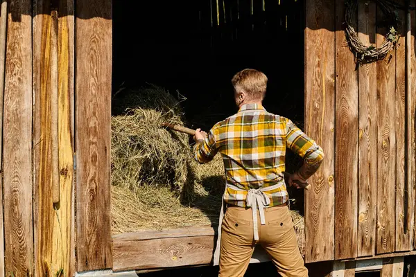 Appealing dedicated farmer in casual attire using pitchfork while working with hay in village — Stock Photo