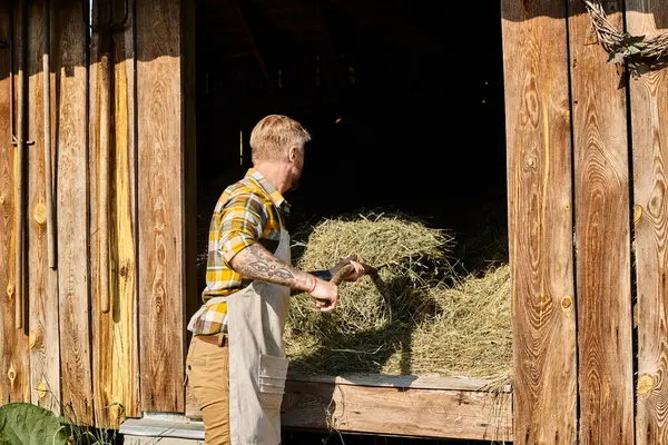 Attraente agricoltore dedicato in abbigliamento casual utilizzando forcone mentre si lavora con fieno nel villaggio — Foto stock