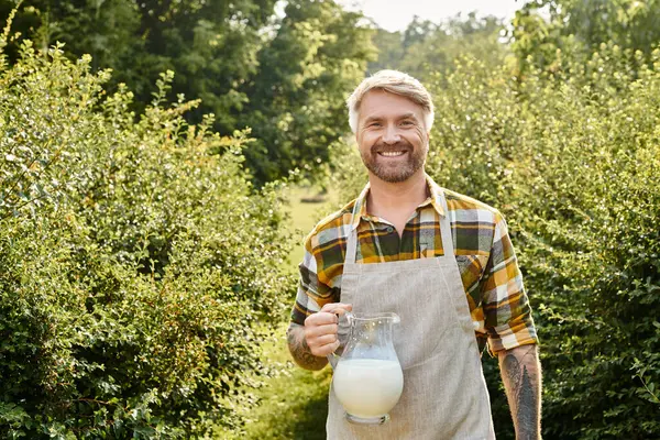 Cheerful handsome man in casual outfit with tattoos holding jar of fresh milk and looking at camera — Stock Photo