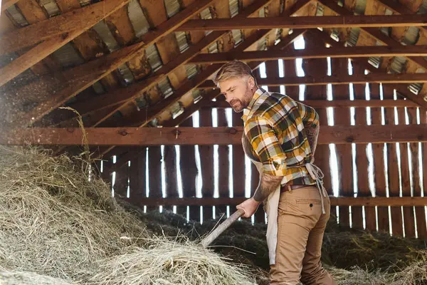 Fröhlicher gutaussehender Mann mit Tätowierungen mit Mistgabel bei der Arbeit mit Heu auf dem Bauernhof — Stockfoto