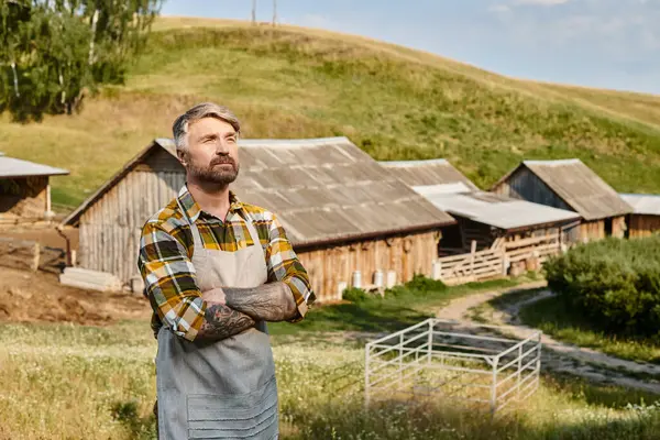 Atraente agricultor moderno dedicado com tatuagens e barba relaxando em sua fazenda e olhando para longe — Fotografia de Stock