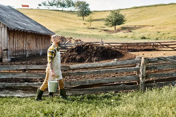Gut aussehender bärtiger Mann mit Tätowierungen auf den Armen, der Eimer mit frischer Milch hält, während er auf seinem Bauernhof ist — Stockfoto