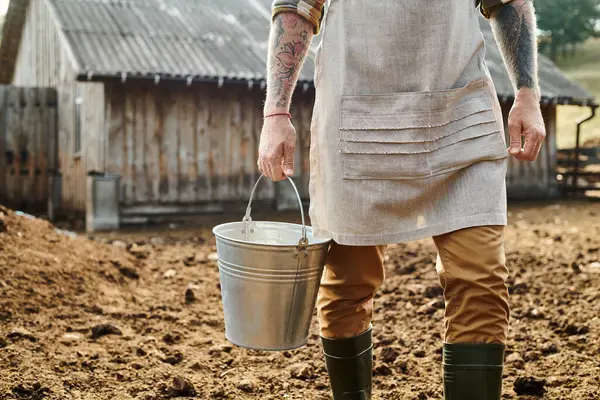Corte vista de adulto dedicado homem com tatuagens em braços segurando balde com leite enquanto na fazenda — Fotografia de Stock