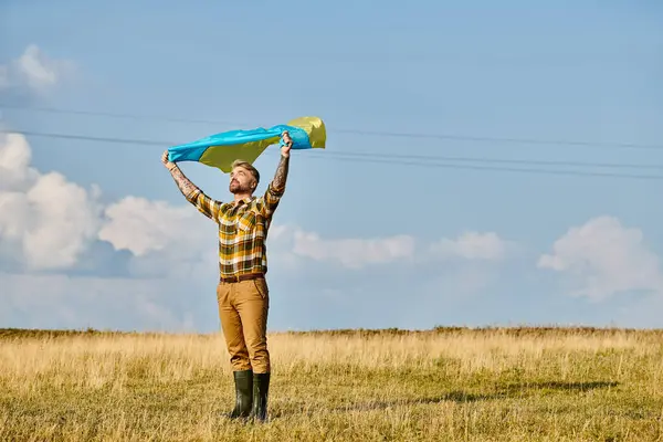 Attraktiver ukrainischer Mann in legerer Kleidung posiert mit Nationalflagge, malerischer Landschaft, modernem Bauern — Stockfoto