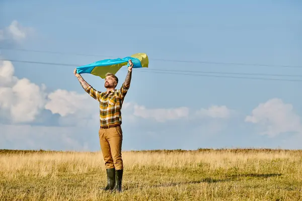 Attraente uomo ucraino in abbigliamento casual posa con bandiera nazionale, paesaggio panoramico, agricoltore moderno — Foto stock