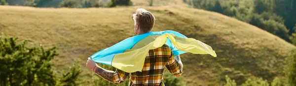 Back view of Ukrainian farmer with tattoos posing with national flag, scenic landscape, banner — Stock Photo