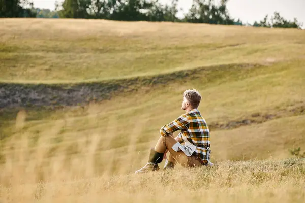 Gutaussehender engagierter Mann mit Bart entspannt auf grünem Frühlingsfeld und schaut weg, moderner Bauer — Stockfoto