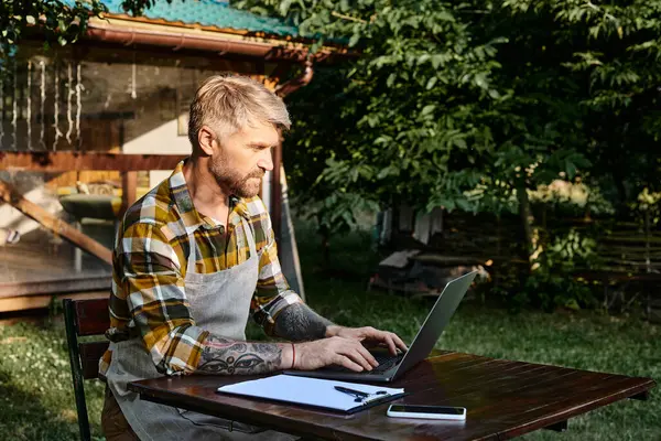 Hombre guapo trabajador con barba usando el ordenador portátil y portapapeles para analizar los recursos en la granja - foto de stock