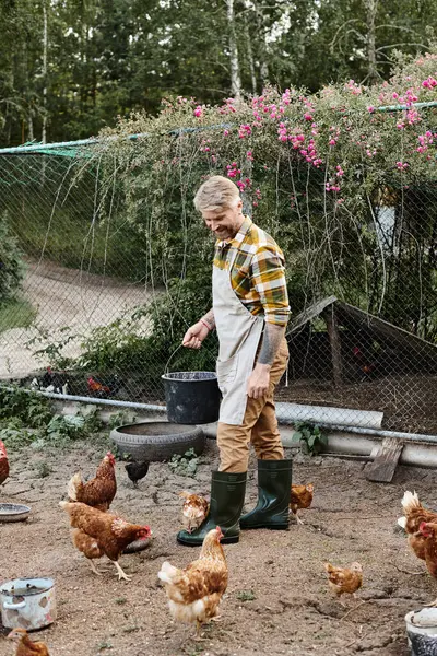 Bell'uomo gioioso con tatuaggi che alimentano i polli nella loro voliera mentre nella sua fattoria nel villaggio — Foto stock