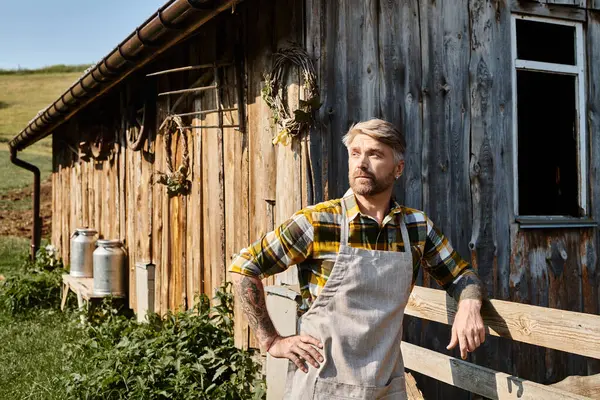 Appealing bearded modern farmer in casual attire with tattoos posing and looking away in village — Stock Photo