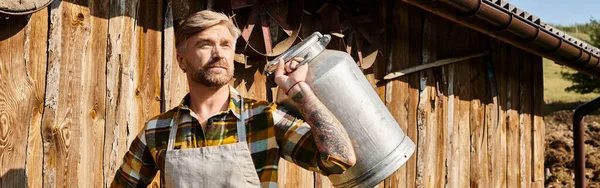 Uomo attraente in abbigliamento casual con tatuaggi in posa con le urne di latte e distogliendo lo sguardo, contadino, banner — Foto stock