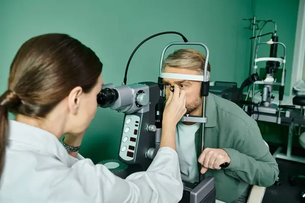 Atractivo médico examinando un ojo de hombre en un entorno profesional. - foto de stock