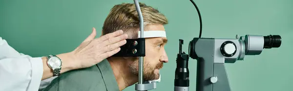El doctor devoto examina los ojos de los hombres a través de un microscopio en un consultorio médico para la corrección de la visión láser. - foto de stock