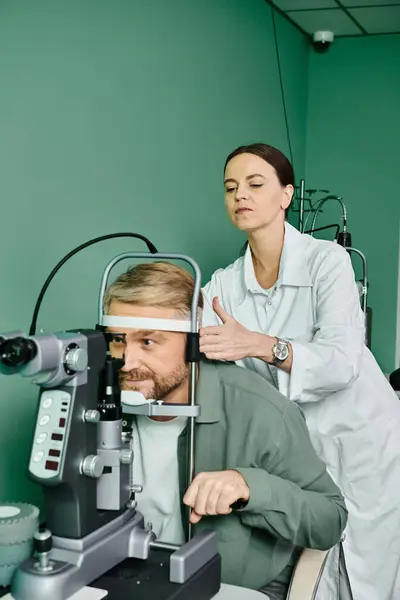 Mujer examina el ojo del hombre con un microscopio en el consultorio médico. - foto de stock