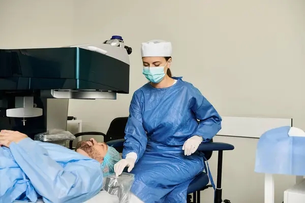Mujer en bata quirúrgica y hombre en silla en la oficina de médicos para la corrección de la visión láser. - foto de stock