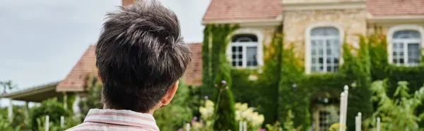 Vista trasera de la mujer madura con el pelo gris posando en frente de su casa de pueblo en Inglaterra, bandera - foto de stock