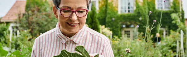 Bella donna matura felice con gli occhiali che lavorano in vivido giardino verde e sorridente gioiosamente, striscione — Foto stock